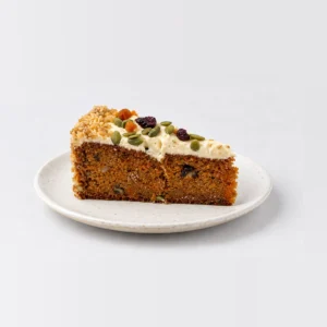 Close-up of the carrot cake slice showing spiced sponge and cream cheese frosting with dried fruit and seeds.