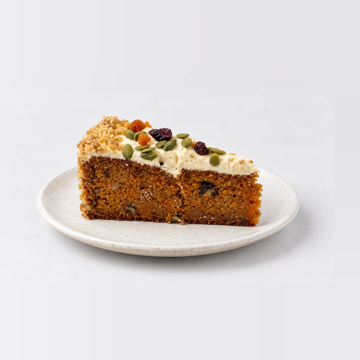 Close-up of the carrot cake slice showing spiced sponge and cream cheese frosting with dried fruit and seeds.