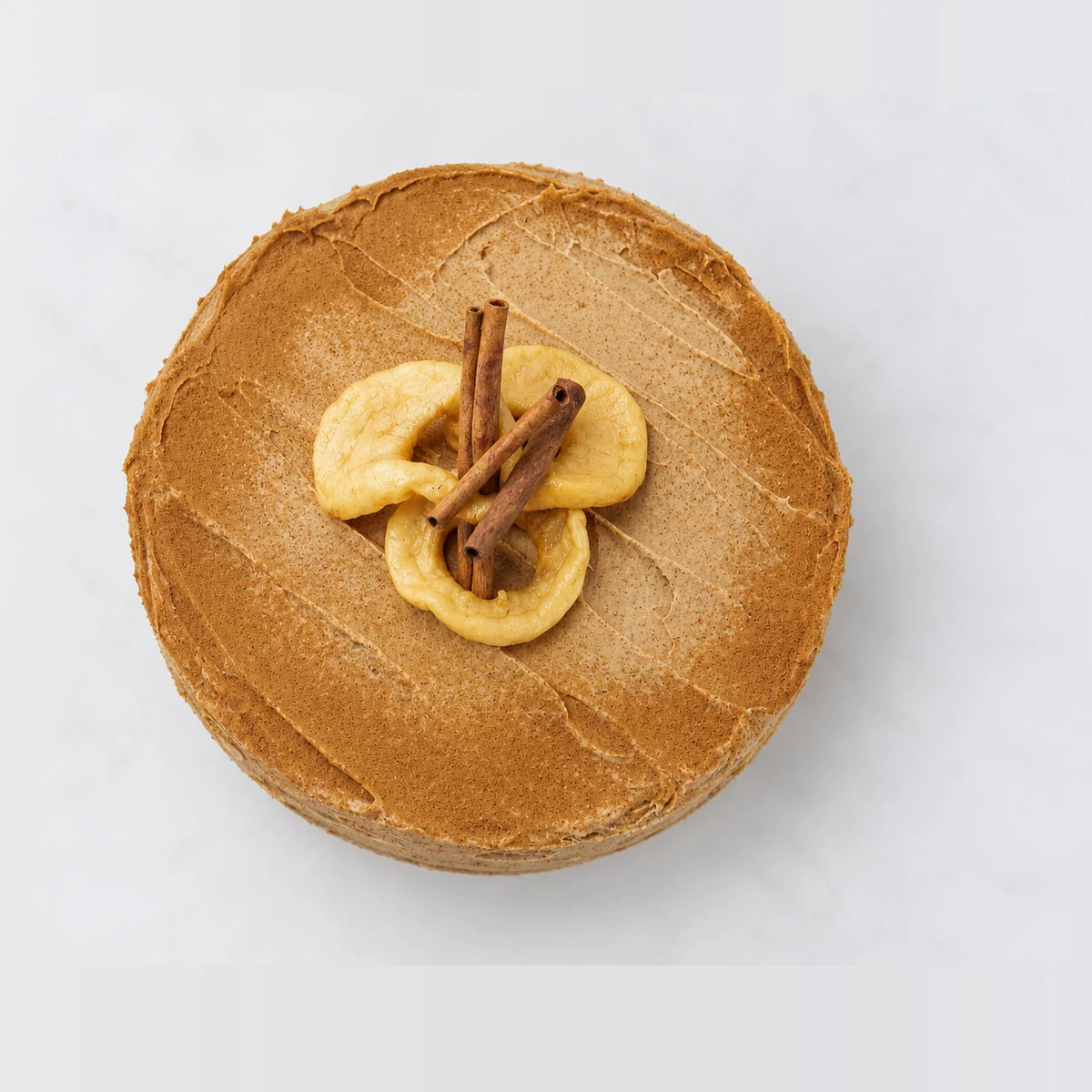 Apple and cinnamon tea cake from above: cinnamon frosting with cinnamon sticks and apple slices in the centre.