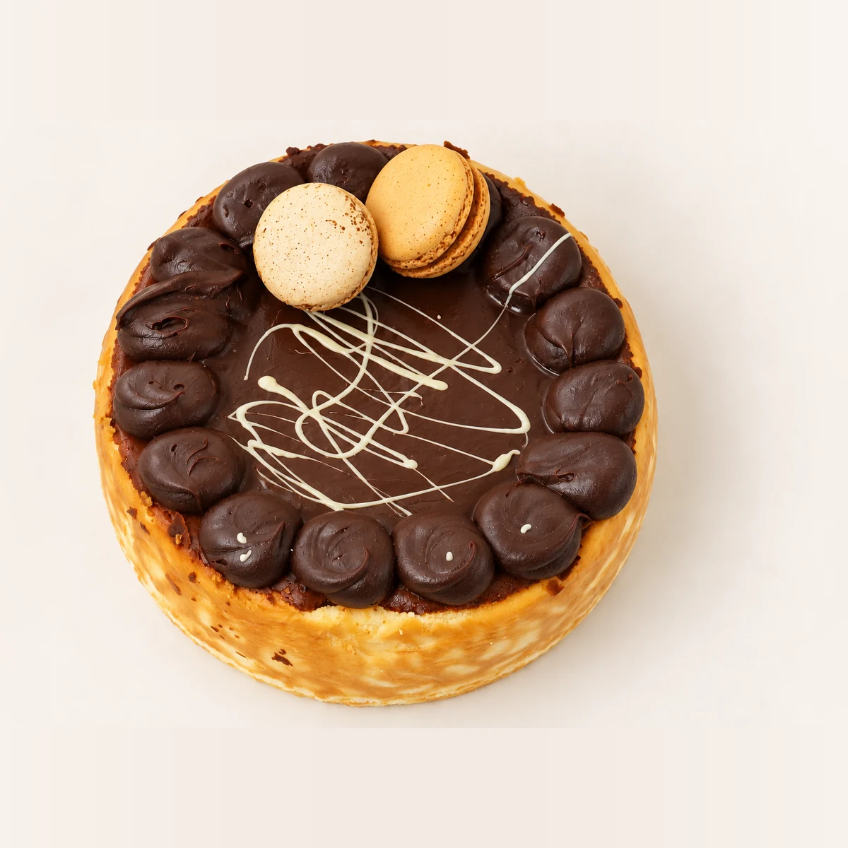 Bailey's cheesecake from above: chocolate layer with white chocolate drizzle, a ring of chocolate rosettes and two macarons.