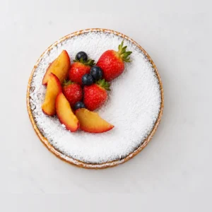 Baked Basque cheesecake from above, dusted with icing sugar with plum slices, strawberries and blueberries on one side.