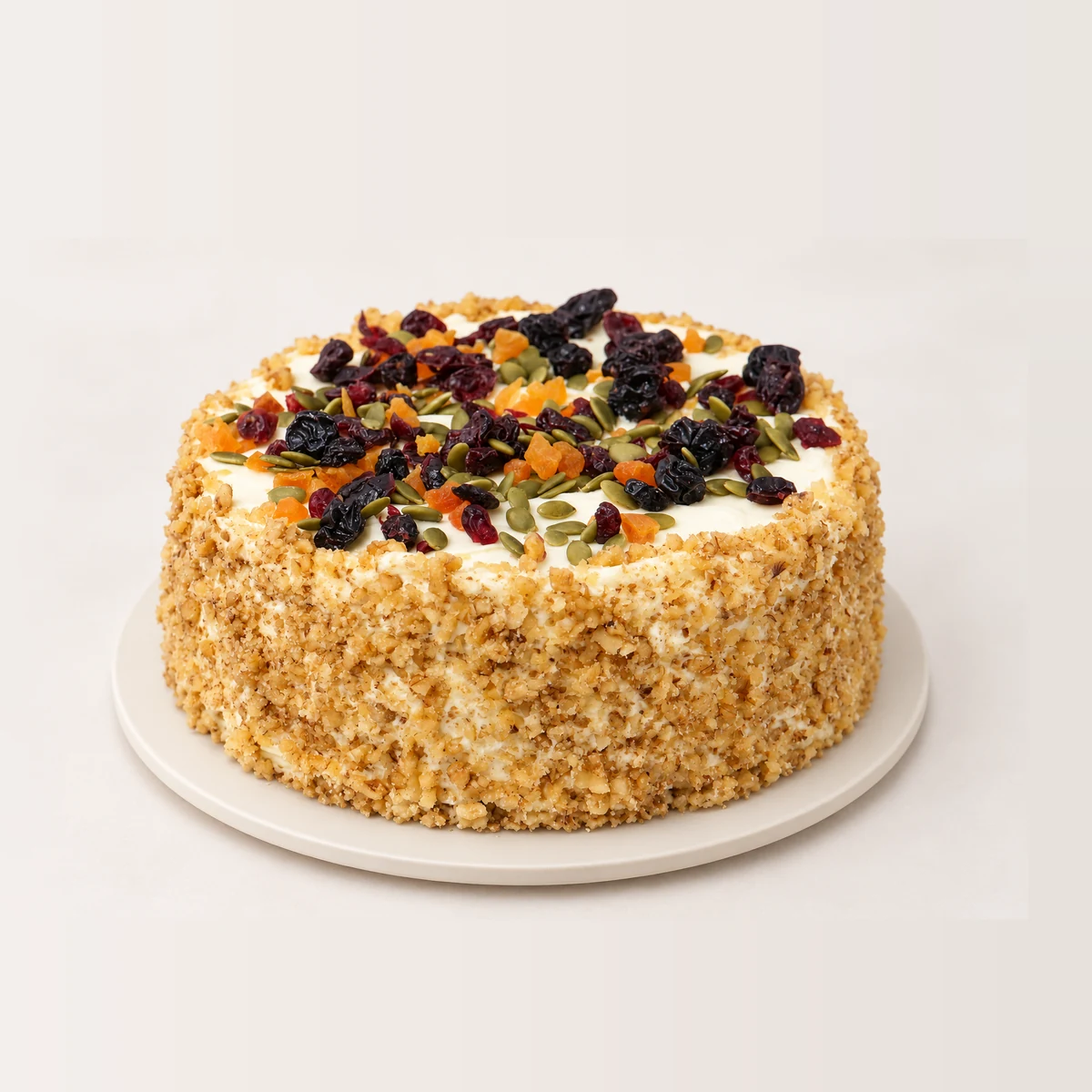 Carrot walnut and orange cake with nut-crumb sides and cream cheese frosting topped with dried fruit and pumpkin seeds.