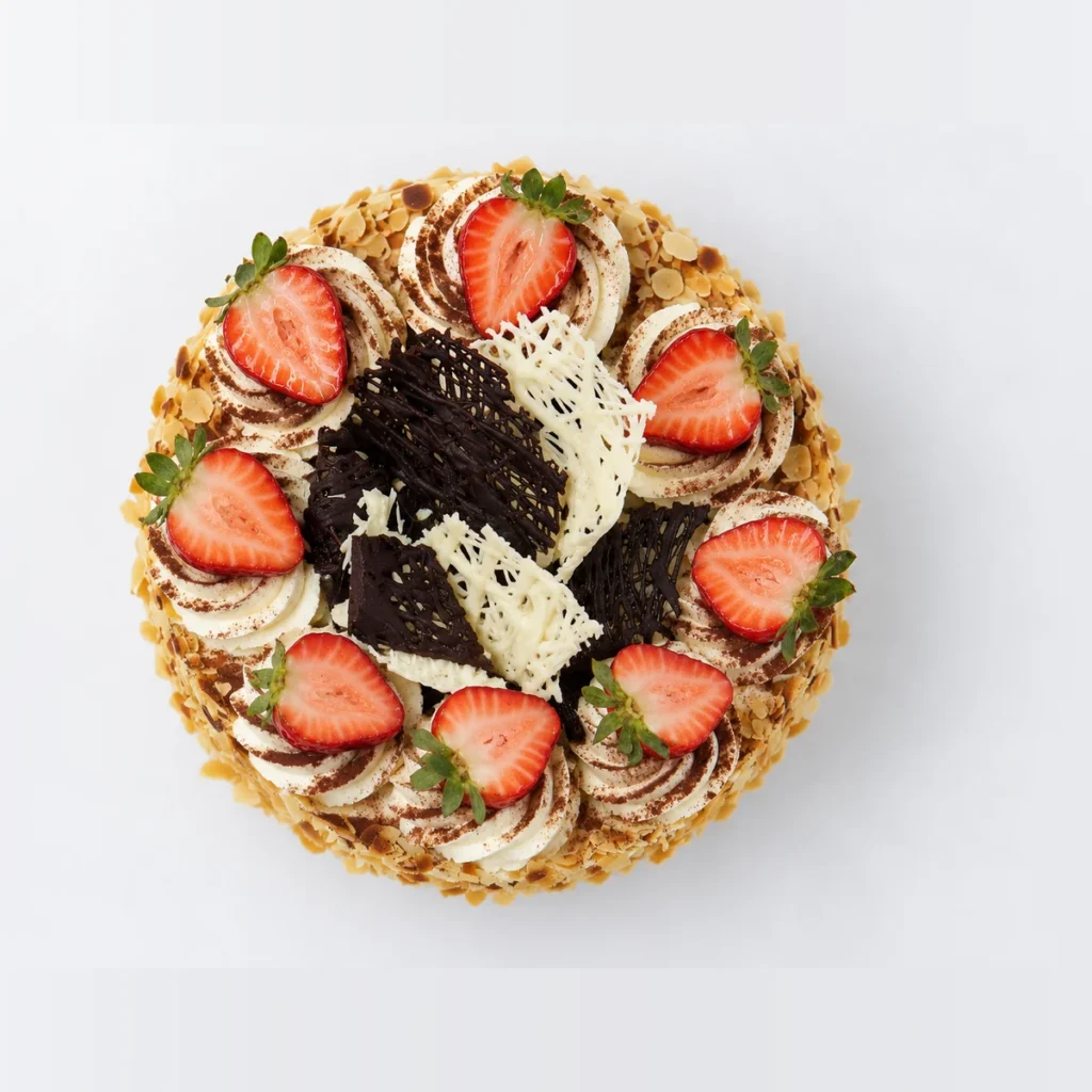 Continental cake from above: cream rosettes, halved strawberries and dark and white chocolate shards.