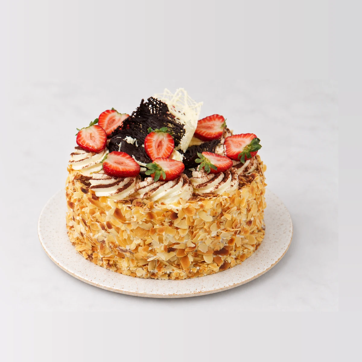 Continental cake coated in toasted flaked almonds, topped with cream rosettes, strawberries and chocolate shards.