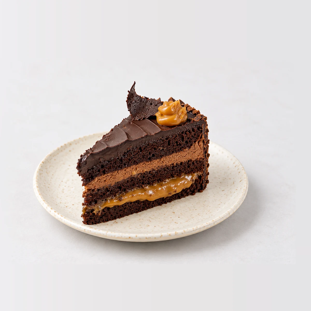 Slice of Marz Bar cake: chocolate cake layers with a chocolate mousse layer and a layer of caramel, covered in chocolate ganache.