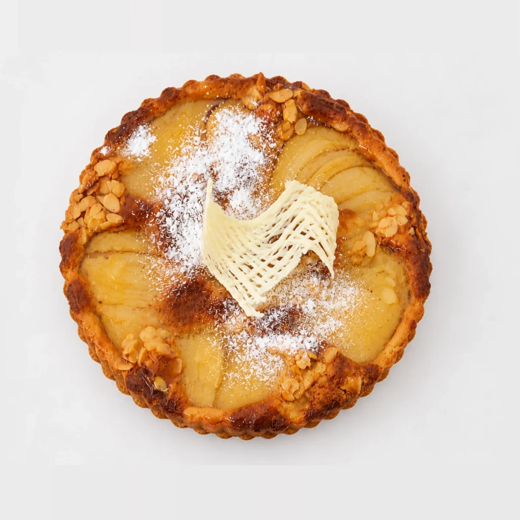 Frangipane tart from above: golden filling with pear slices, flaked almonds, icing sugar and a white chocolate decoration.