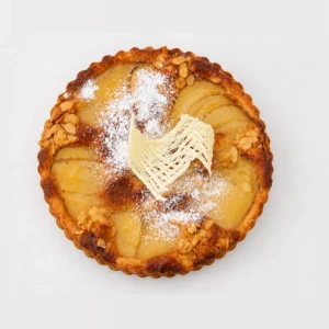 Frangipane tart from above: golden filling with pear slices, flaked almonds, icing sugar and a white chocolate decoration.