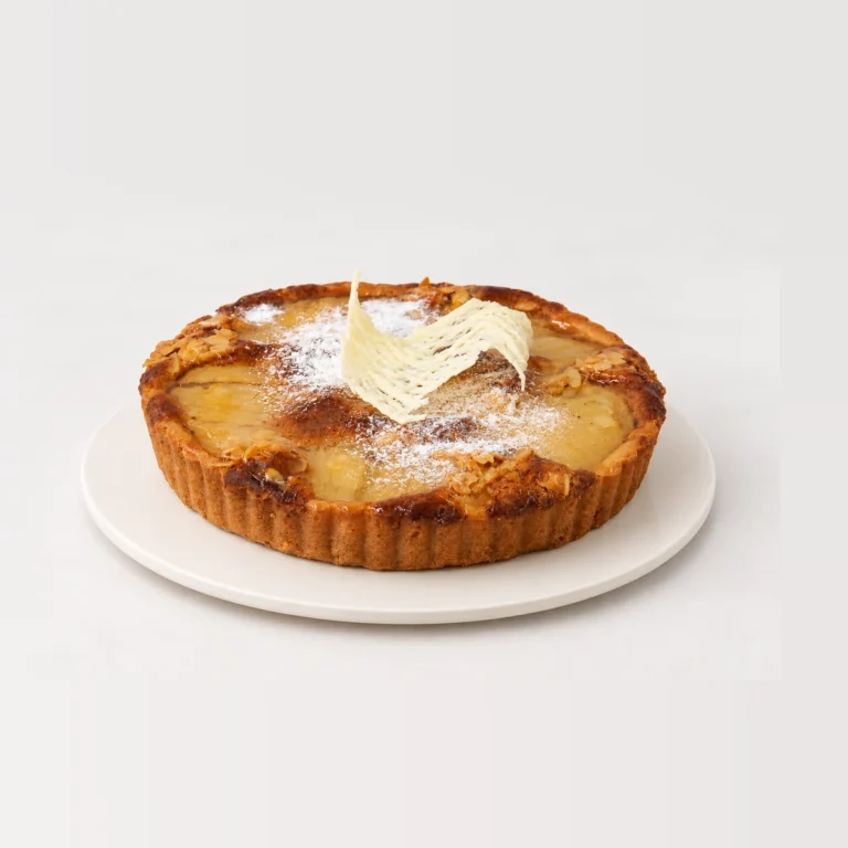 Frangipane tart in a fluted pastry shell, with a golden top dusted with icing sugar and a white chocolate decoration.
