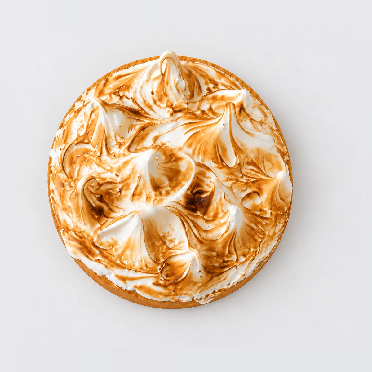 Lemon meringue tart from above: swirled meringue peaks caramelised to golden brown.