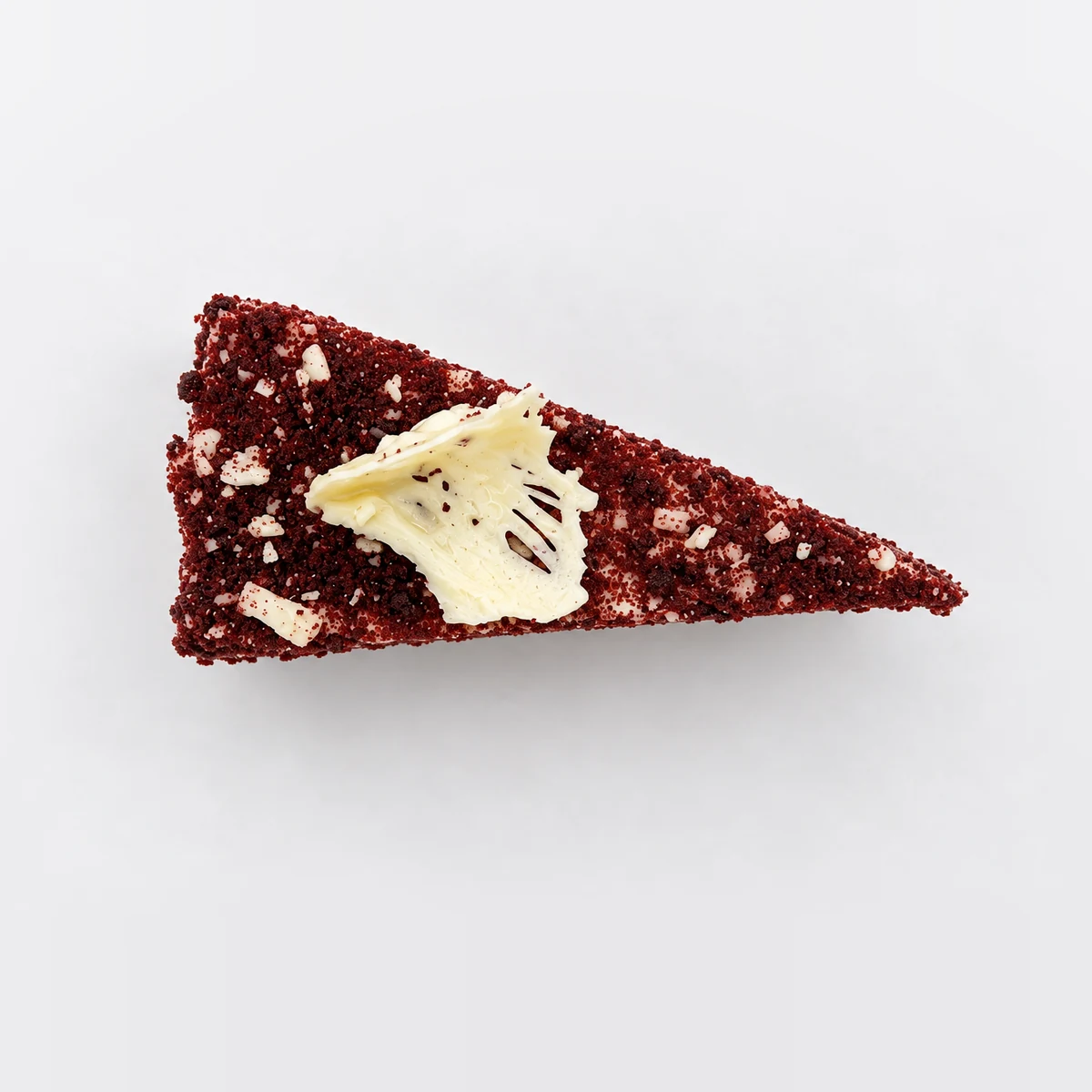 Red velvet slice from above, covered in red velvet crumb with a white chocolate curl.
