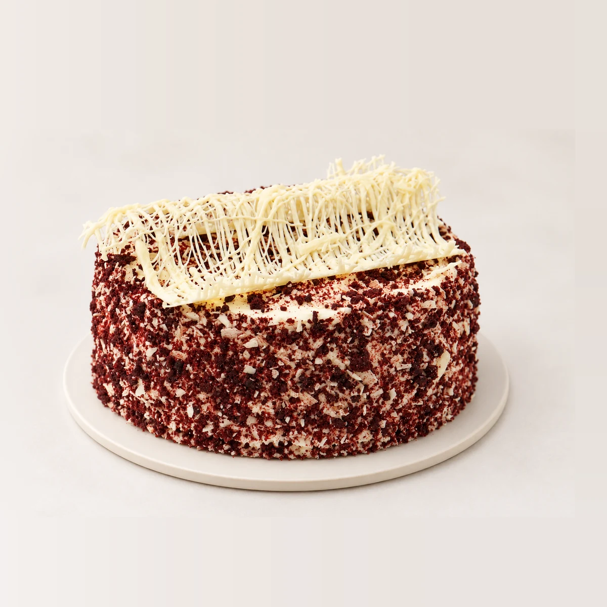 Red velvet cake coated in red velvet crumb, topped with a white chocolate decoration.