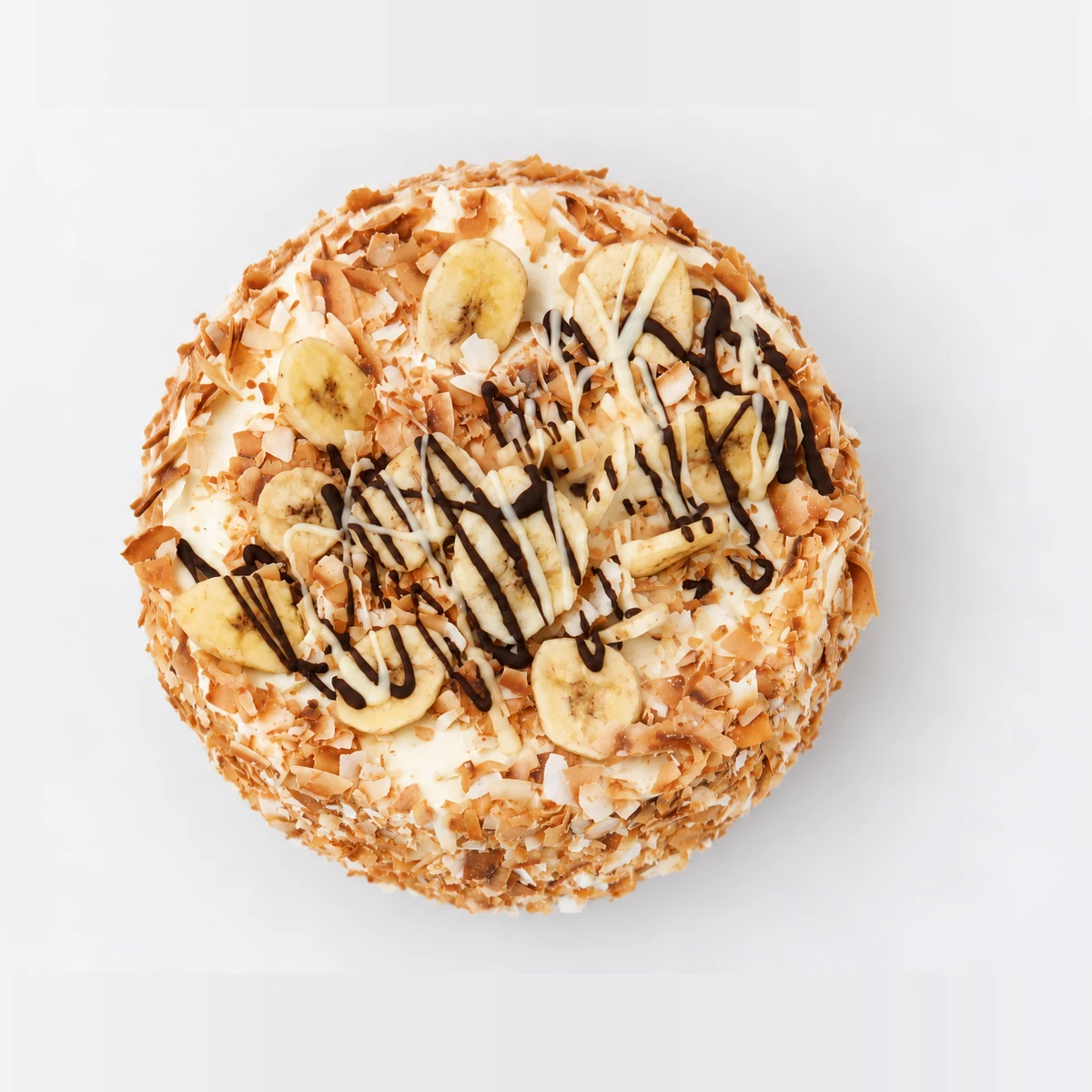 Tropical banana and coconut cake from above: banana slices and chocolate drizzle on cream, with toasted coconut around the edge.