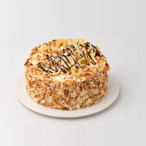 Tropical banana and coconut cake coated in toasted coconut flakes, topped with banana slices and a chocolate drizzle.