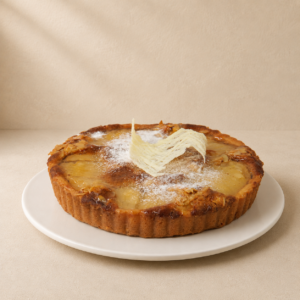 Frangipane tart in a pastry shell with poached pear, a dusting of icing sugar and a chocolate tuile.