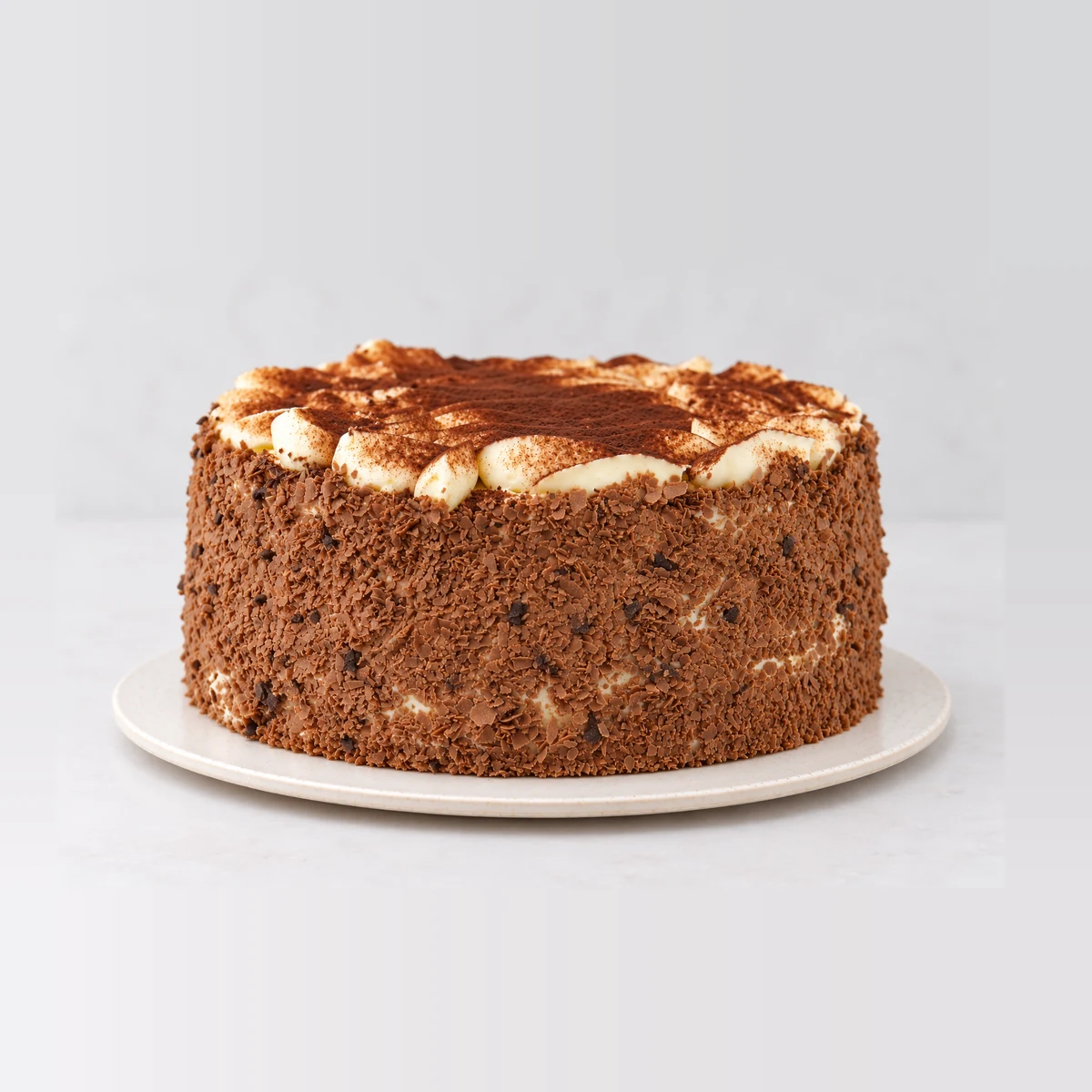 Side view of the tiramisu cake showing chocolate-crumb sides, cream and a cocoa-dusted top.