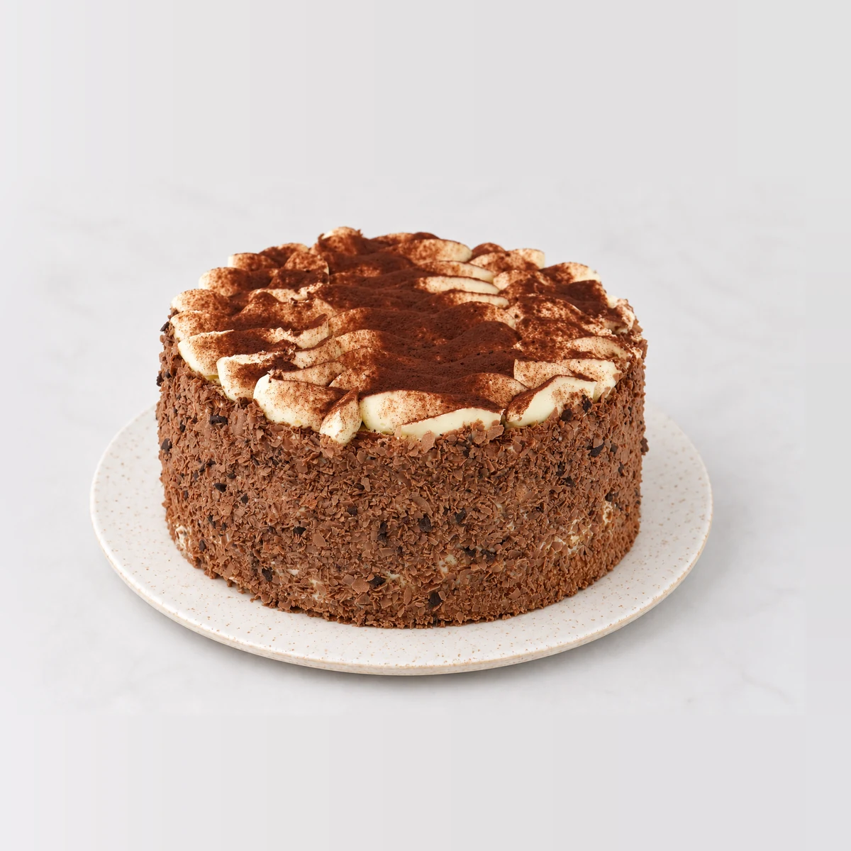 Tiramisu cake with chocolate-crumb sides and swirls of cream on top dusted with cocoa.